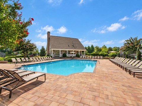 A pool surrounded by lounge chairs and a house in the background.