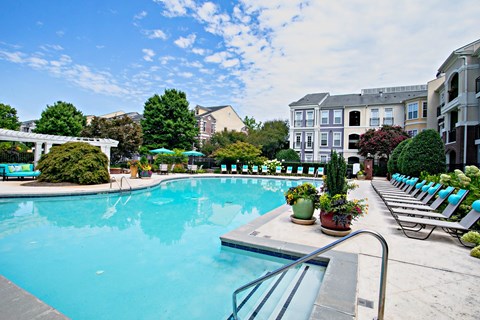 A large swimming pool surrounded by lounge chairs and potted plants.