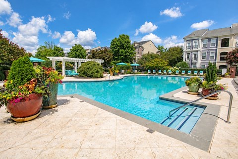 A pool surrounded by a patio and a garden.