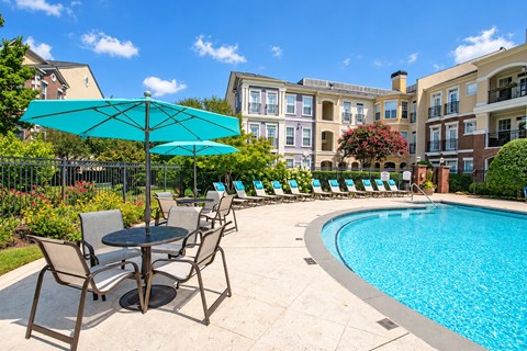 A pool area with chairs and umbrellas in front of a building.