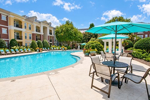 A pool area with a table and chairs and a blue umbrella.