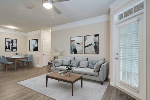 A living room with a grey couch, a dining table with chairs, a coffee table, and a ceiling fan.