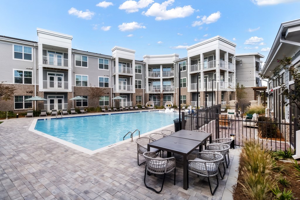 a swimming pool with a table and chairs in front of an apartment building