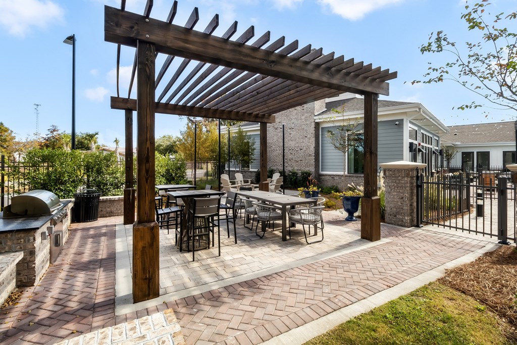 a brick patio with tables and chairs under a wooden pergola