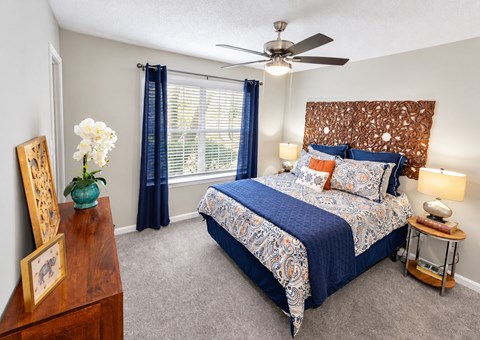 A bedroom with a bed, a ceiling fan, and a nightstand with a lamp.
