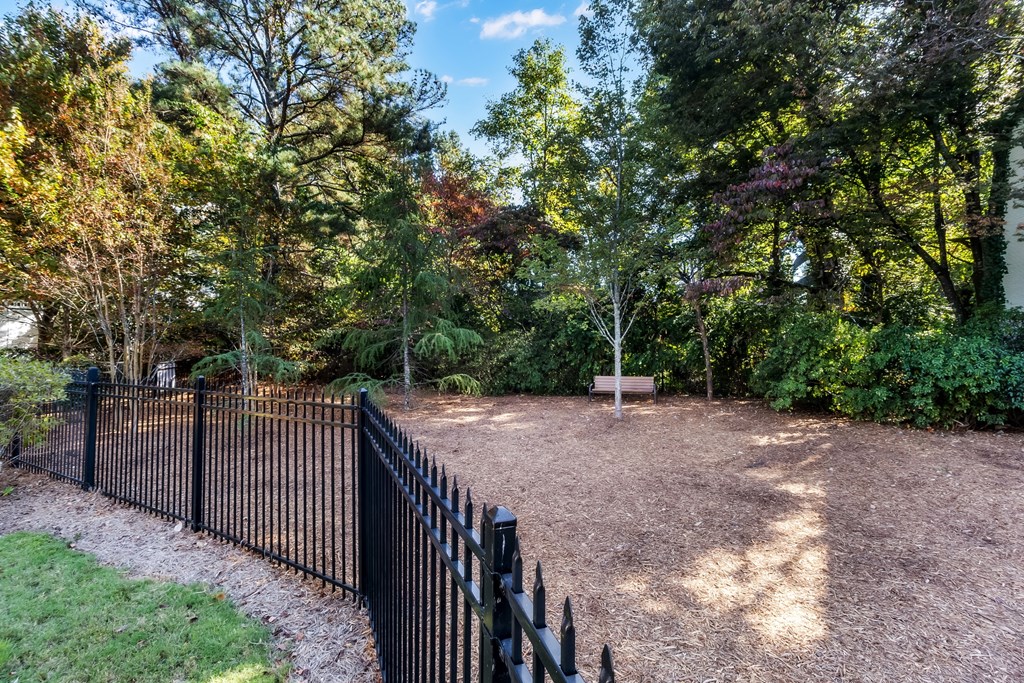 A black metal fence surrounds a dirt area with trees in the background.