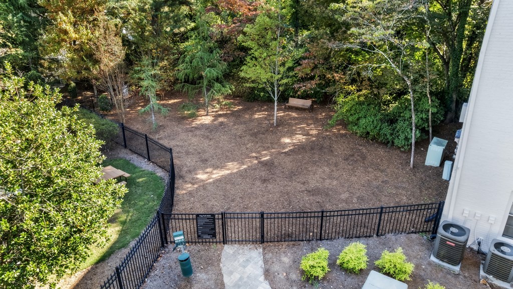 A backyard with a black fence and a green trash can.