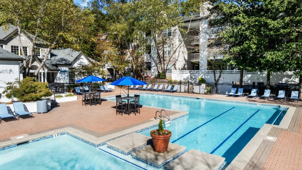 A pool area with a blue umbrella and chairs.