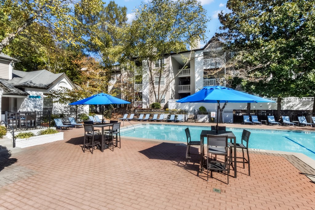 A pool area with chairs and umbrellas is surrounded by trees.