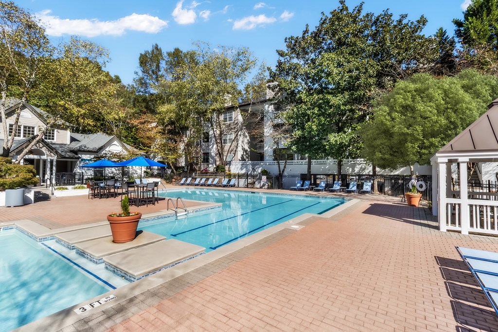 A large outdoor swimming pool surrounded by a brick patio and trees.