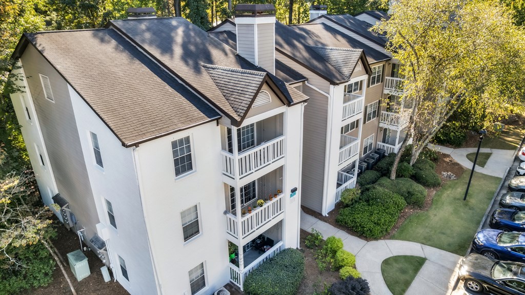 An aerial view of a white apartment building with a brown roof and a parking lot in front.