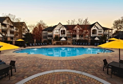 A large outdoor swimming pool surrounded by a brick patio and lounge chairs.