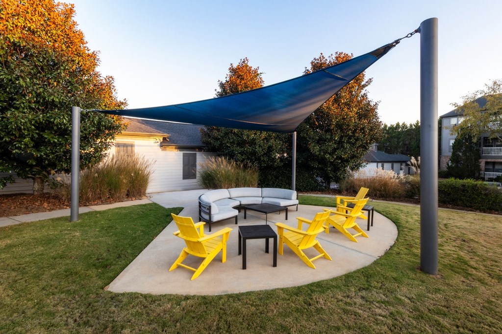 a patio with yellow chairs and a table and a blue canopy at The Reserve at Sugarloaf Apartments, Duluth