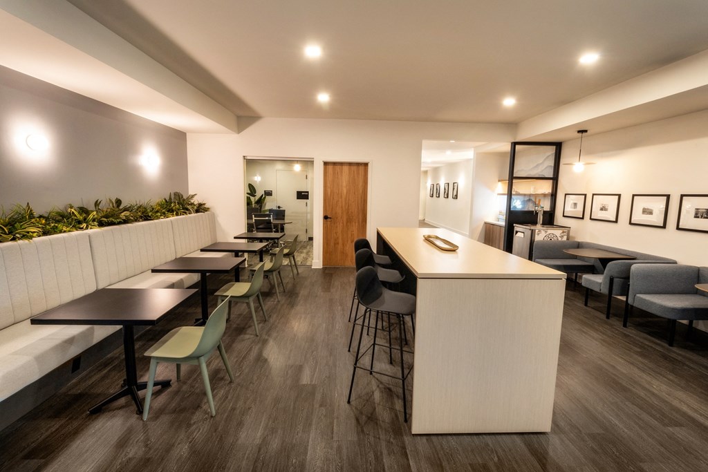 a communal area with tables and chairs and a kitchen with a bar and chairs