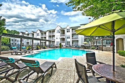 A pool area with chairs and a table with a yellow umbrella.