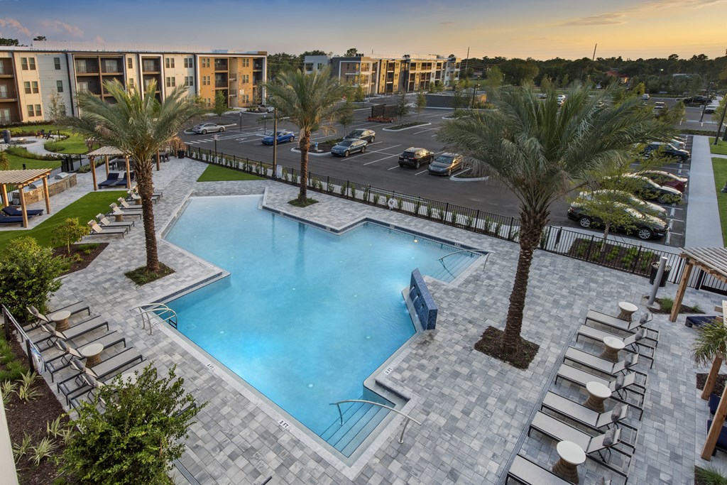 a swimming pool with chaise lounge chairs and palm trees in front of a parking lot