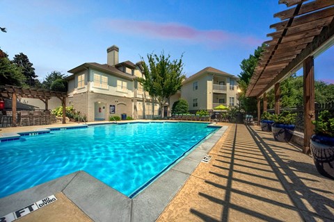 A large swimming pool in front of a house with a wooden pergola.