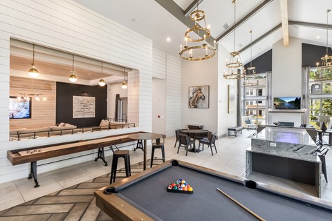 A pool table is in the middle of a room with a bar and a television.