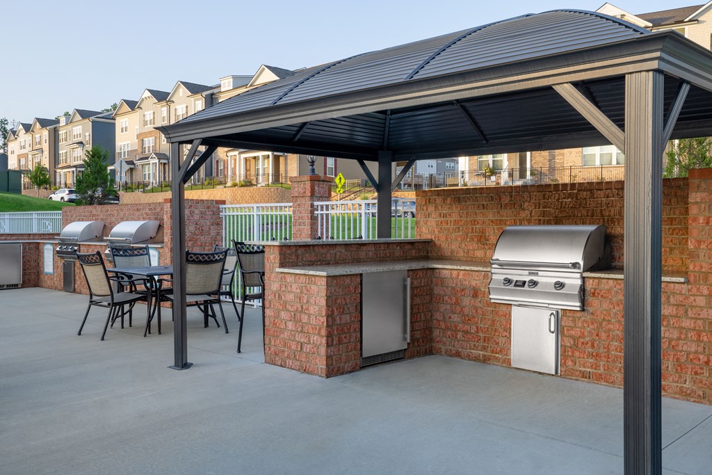 an outdoor kitchen with a barbecue grill and a table and chairs under an awning