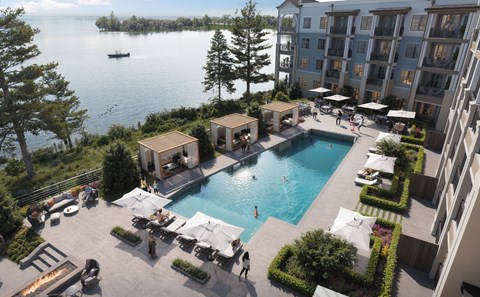 A large swimming pool surrounded by lounge chairs and umbrellas with a lake and trees in the background.