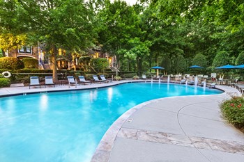 a swimming pool with chaise lounge chairs and trees in the background - Photo Gallery 10