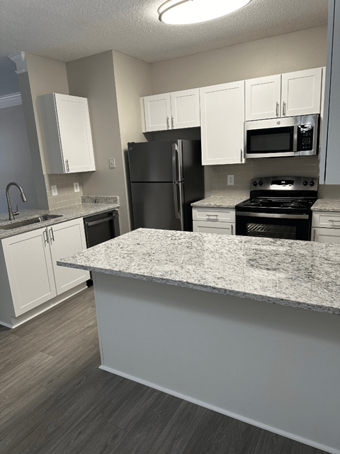 A kitchen with a black refrigerator, white cabinets, and a granite countertop.