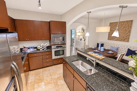 A kitchen with a refrigerator, microwave, oven, sink, and a table with chairs.