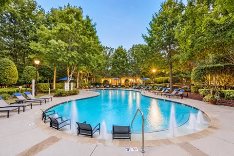A round swimming pool surrounded by trees and lounge chairs.