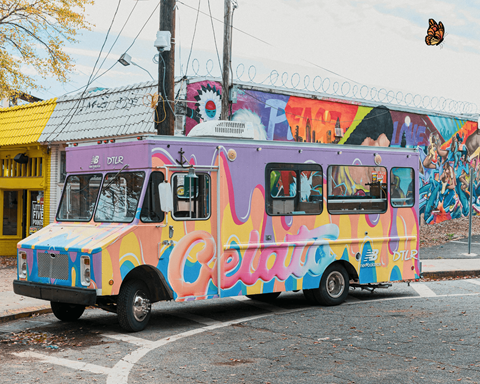 A colorful bus with the word "Celeste" written on it is parked in front of a building with a mural.