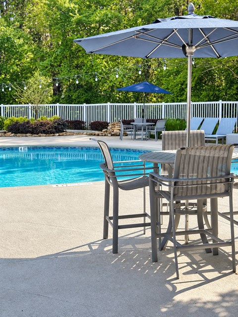 A poolside table with chairs and umbrellas.
