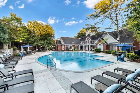A large outdoor swimming pool surrounded by lounge chairs and trees.