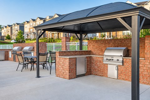 A patio with a grill and chairs under a black awning.