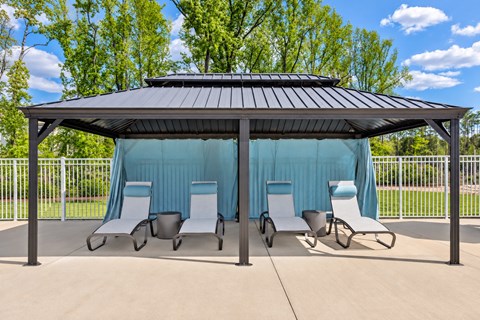 A gazebo with a black roof and white chairs is surrounded by a fence.