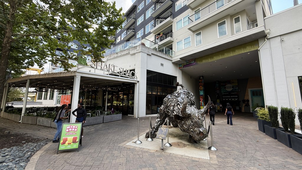 A sculpture of a bull is in the foreground of a shopping area.