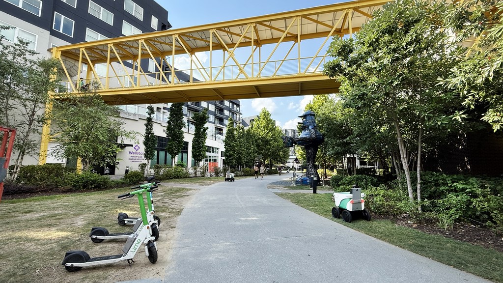 A yellow pedestrian bridge over a walkway with green scooters parked on the side.