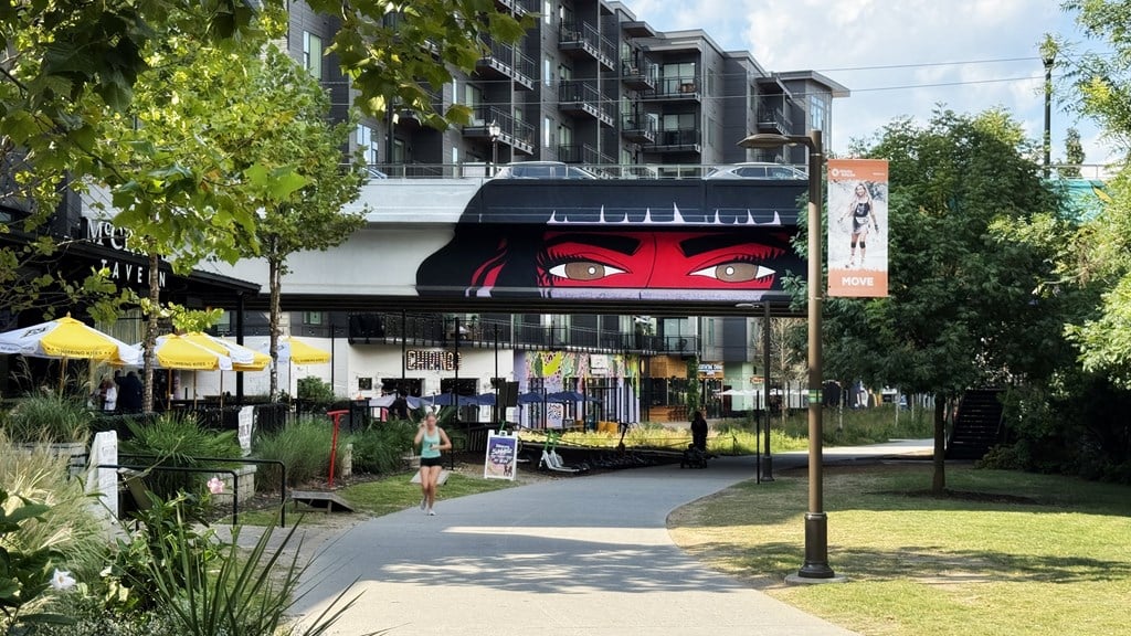 A woman is walking on a sidewalk in front of a building with a large red face on it.