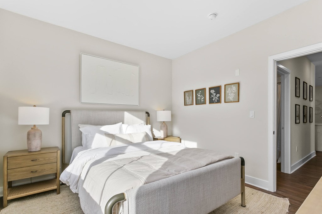 A bedroom with a large bed, a nightstand with a lamp, and pictures on the wall.