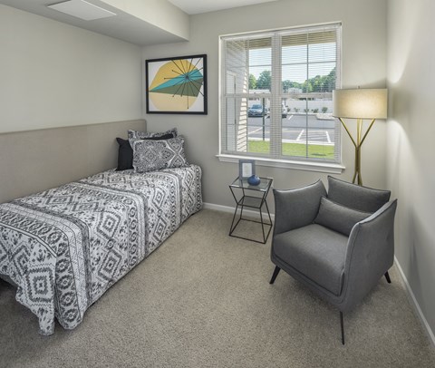 a bedroom with a bed and a chair and a window at Eden & Main 55+ Apartments, Southington, CT