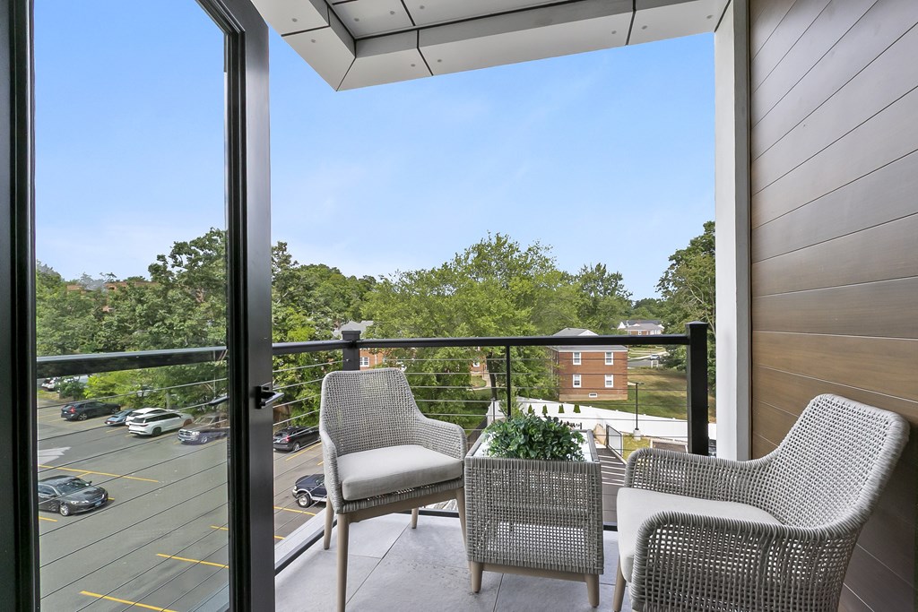 Two chairs on a balcony overlooking a parking lot and trees.