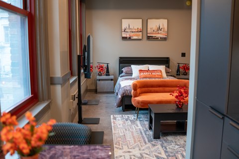 A bedroom with a bed, orange chair, and a window.