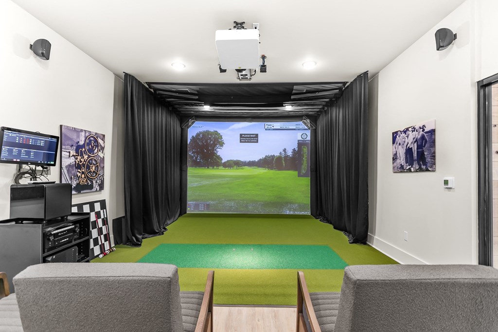 A room with a green carpet and a screen showing a golf course.