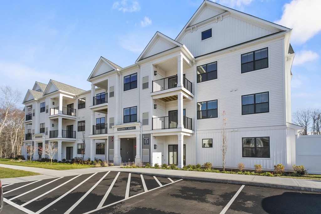A large white apartment building with a parking lot in front.