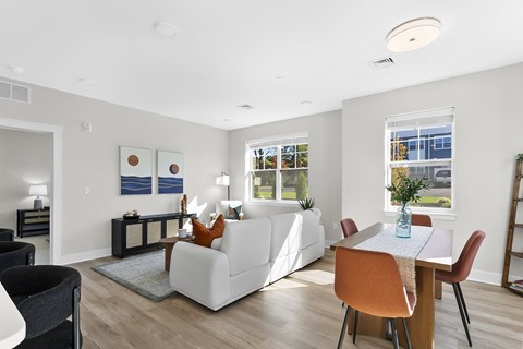 A modern living room with a white sofa, a wooden dining table, and a black chair.