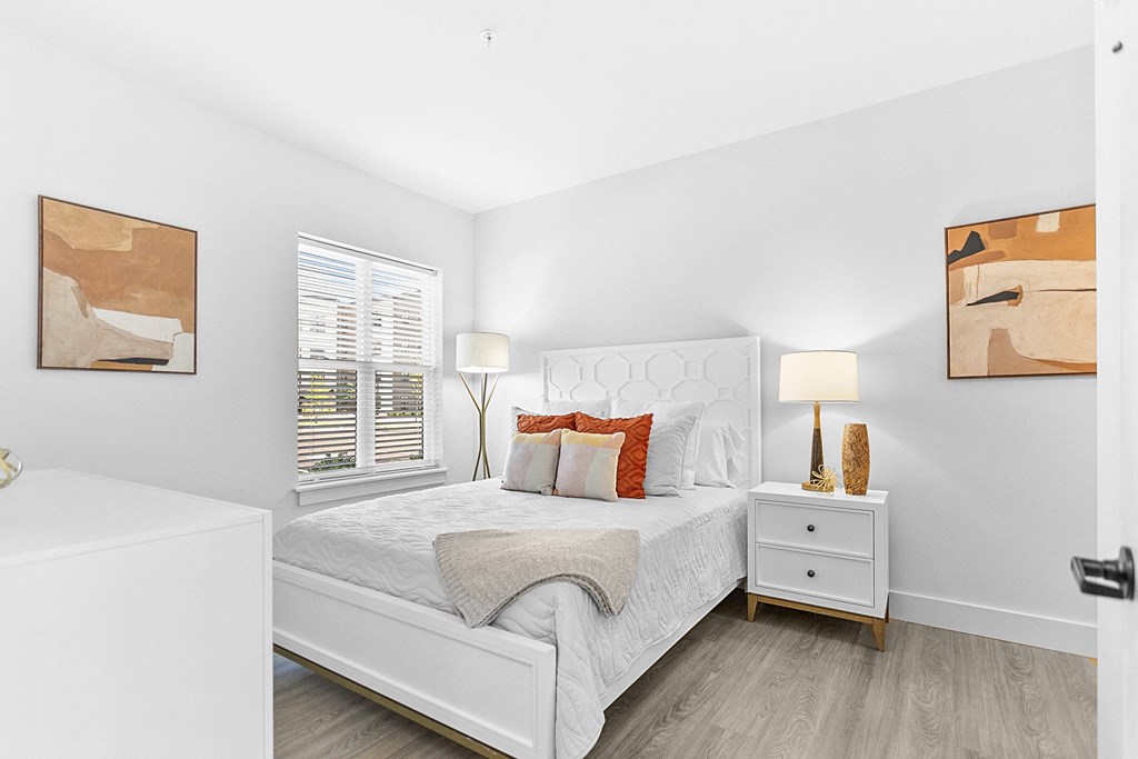 A white bedroom with a bed, nightstand, and two framed artworks on the wall.