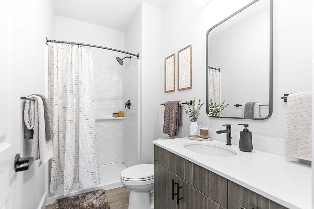 A bathroom with a white toilet, a sink, a mirror, and a shower with a white curtain.