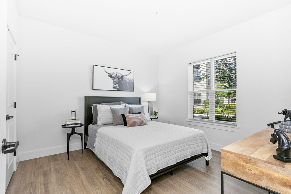 A bedroom with a bed, nightstand, and a painting of a cow on the wall.