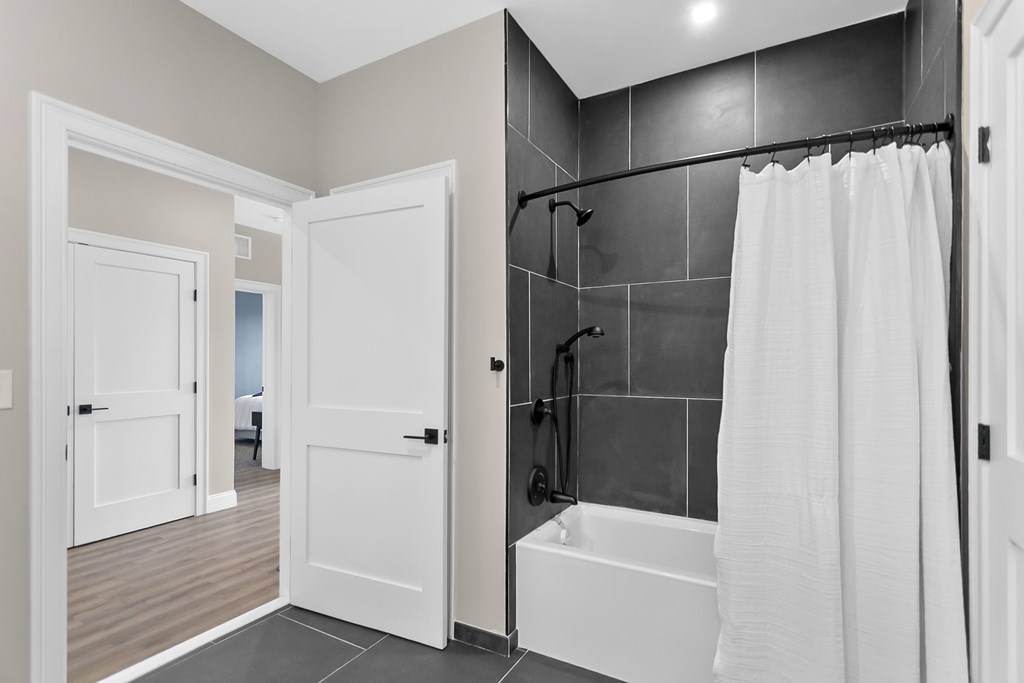 A white bathroom with a black shower head and a white bathtub.
