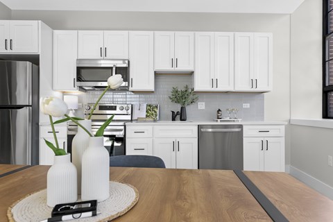 A kitchen with white cabinets and a wooden table with two vases on it.