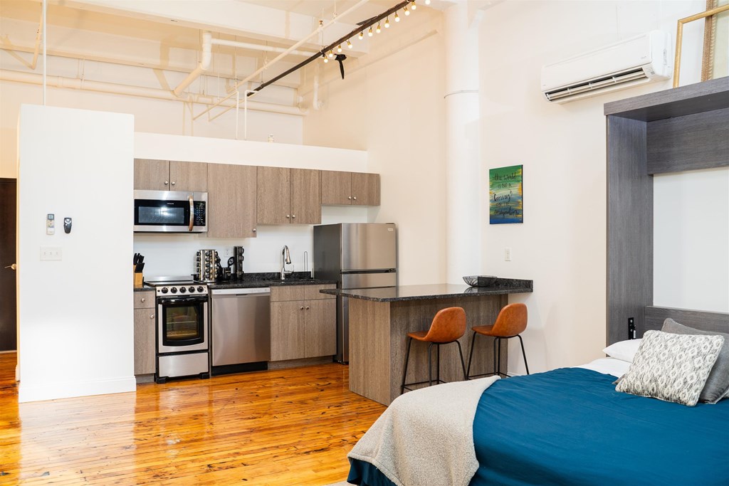 A bedroom with a bed, a kitchen area, and a dining area.