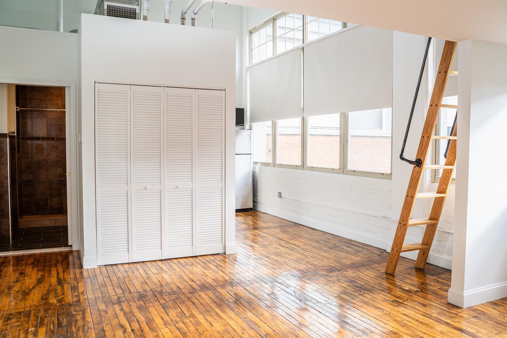 A room with a wooden floor and a white wall with a ladder leaning against it.